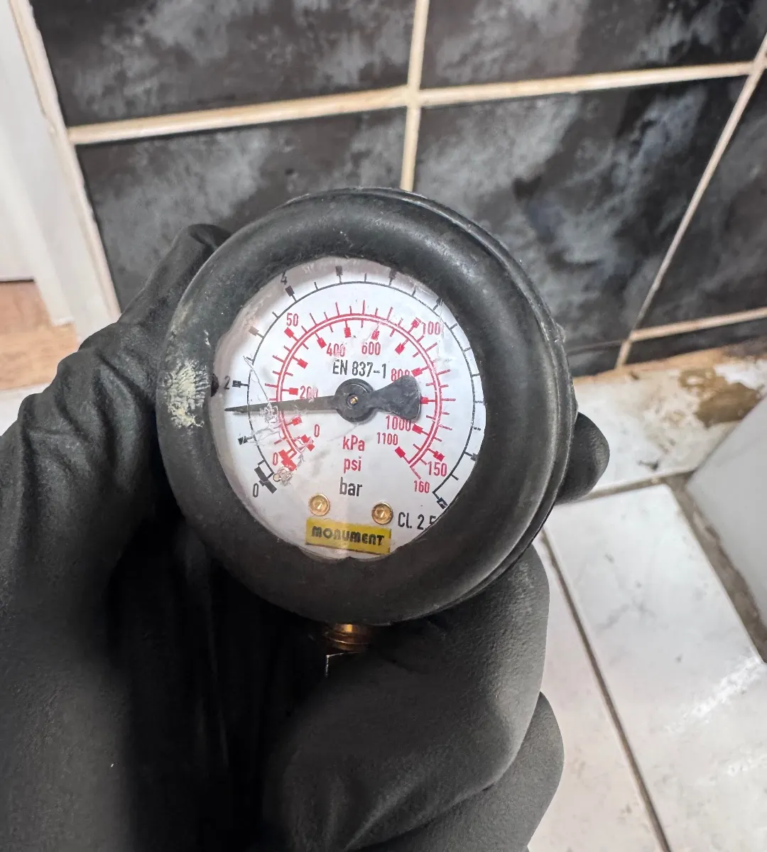 Pressure test gauge held at a bathroom pipe during a leak investigation